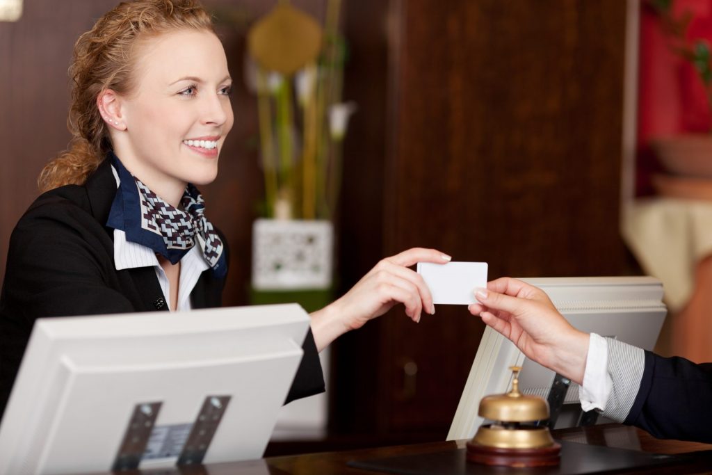 The receptionist smiles and gives the guest a room access card